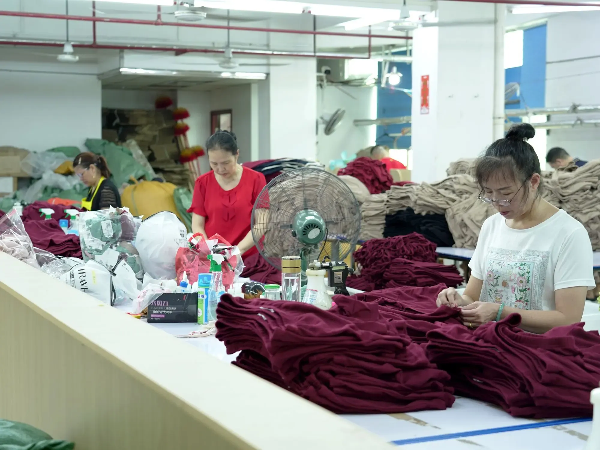 Staff trimming and checking finished garments at a long table