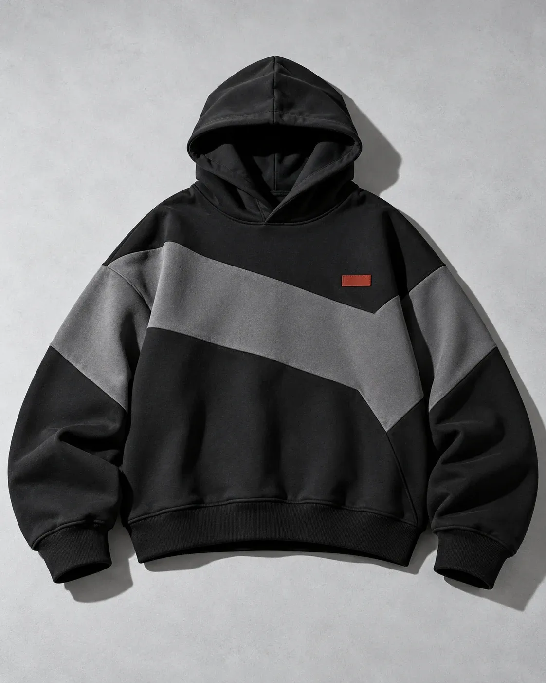 Boxy black pullover hoodie with angular gray panels and a small red patch